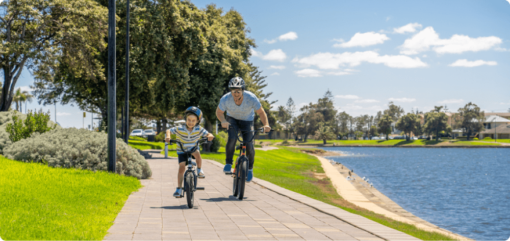 A child and parent ride on their bikes along a pathway by the water.